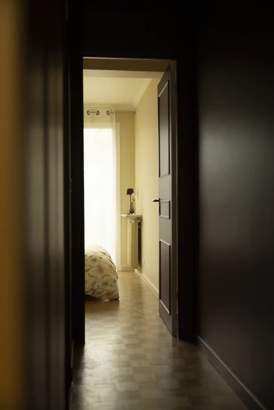 Dark corridor opening onto a bright bedroom, herringbone parquet